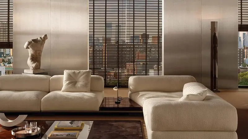 Two cream modular sofas face each other in a city apartment, a marble torso standing on a plinth behind them.