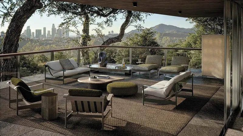 On a covered terrace above a wooded hillside, low outdoor seating and a stone table look out to a distant skyline.