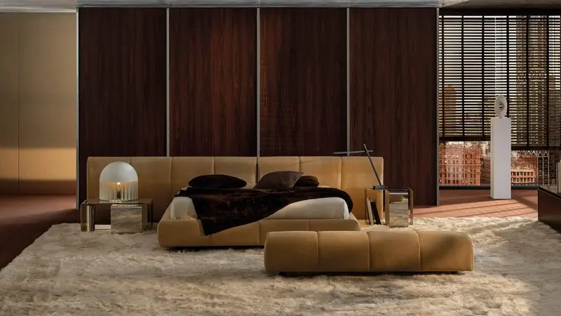 Tan leather headboard panels and a long bench sit on a deep pale rug in a rosewood-lined bedroom.