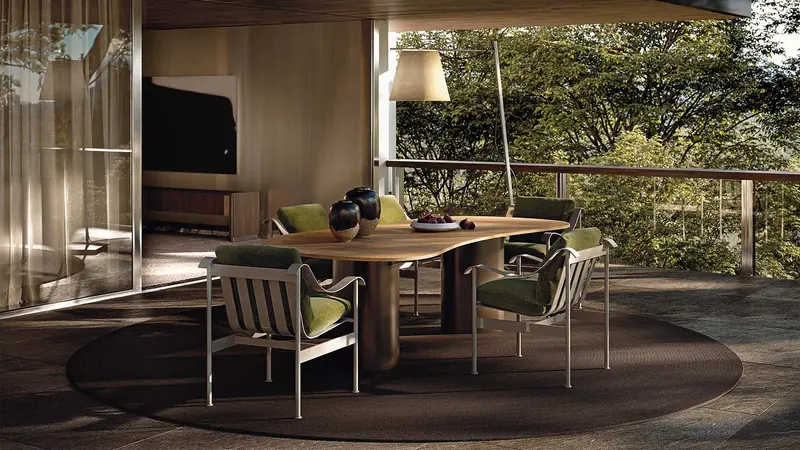 A shaped teak dining table and green-cushioned armchairs sit on an open terrace over a wooded valley.