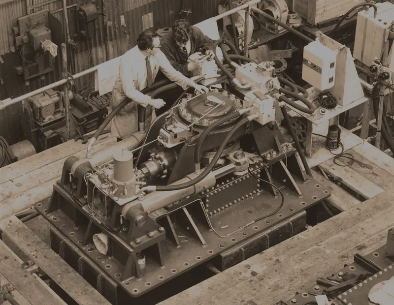 Two engineers fit a stabiliser actuator to a test rig on the factory floor, an archive photograph from the Sperry/Naiad fin-stabiliser lineage the company traces its hydraulic actuator design back to.