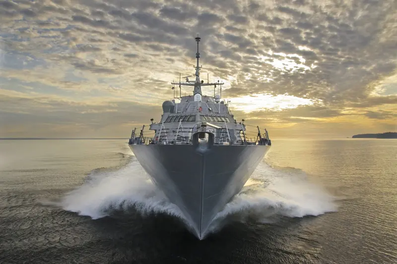 A Freedom-class littoral combat ship drives its bow through a following sea, the kind of naval hull where Naiad's ride control systems are specified across more than fifty navies and coast guards.