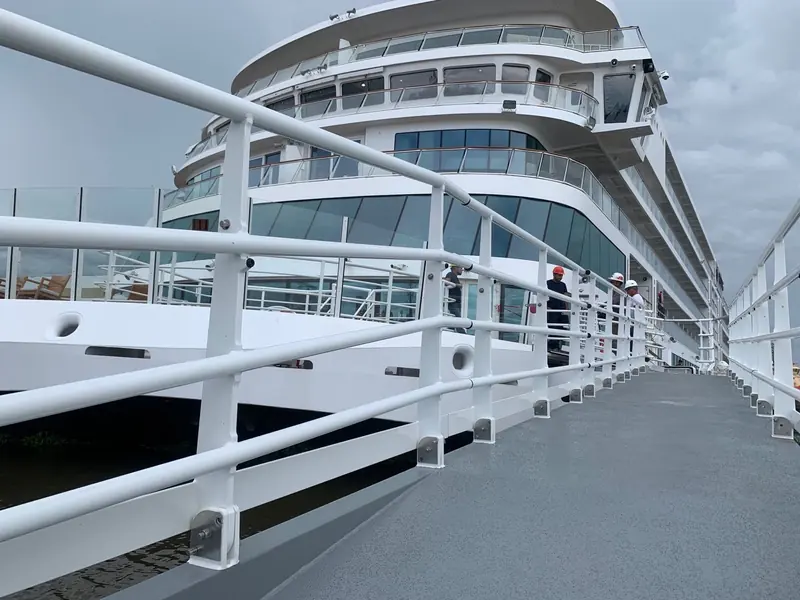 Crew and a shipyard inspector walk down a boarding gangway rigged from a cruise ship's shell door to the quay below.