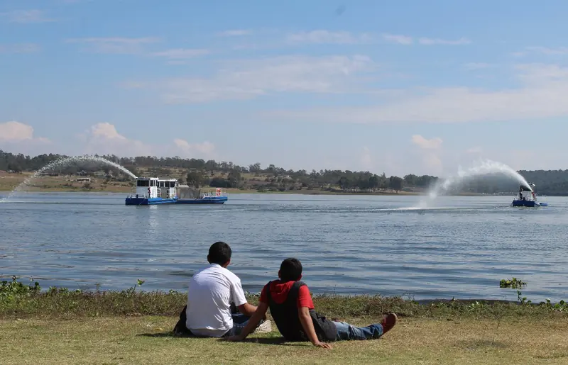 A Scavenger 2000 harvester at work on a lake, spraying a long arc of water while two boys watch from the bank. The type is built around a Northern Lights generator set.
