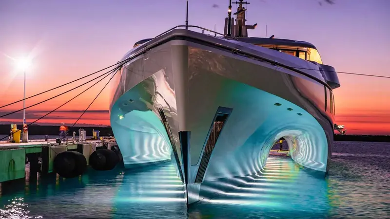 A yacht's transom glows blue-green at dusk from Ocean LED underwater lights recessed below the waterline, the light spilling out across the marina water at the stern.