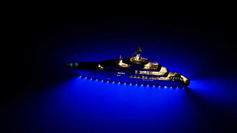 A superyacht at anchor after dark, its Ocean LED underwater lights turning the water around the hull a deep blue that lights the waterline from bow to stern.