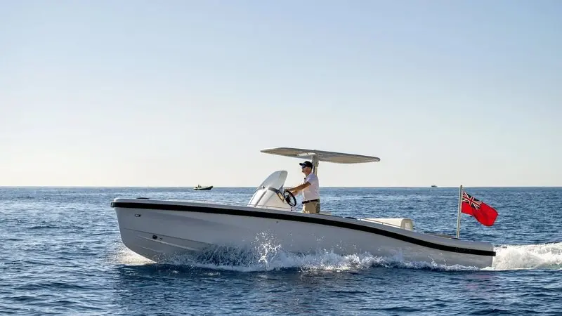 Standing at an open helm under a cantilevered hardtop, a driver takes a Pascoe tender across calm water.