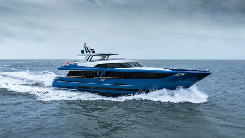 A blue hulled motor yacht runs through a grey sea under an overcast sky.