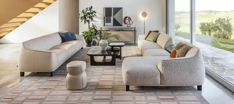 A leather sofa and a boucle sectional face each other across a graphic rug in a bright living room overlooking open countryside.