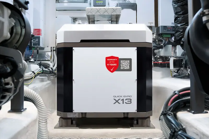 A Quick Gyro X13 stabiliser installed between the hull stringers of a yacht's machinery space, its white composite housing bearing a four-year warranty sticker and QR code