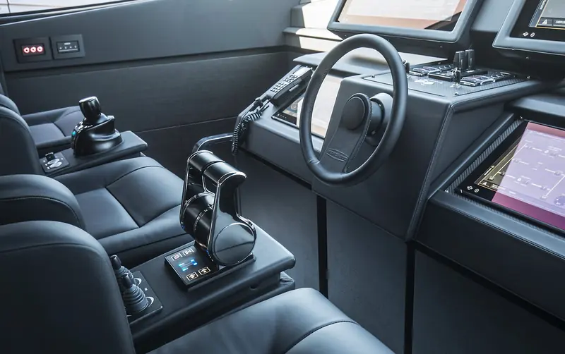 A yacht helm station with twin black joystick docking controls in the armrests ahead of the leather-trimmed seats, multifunction displays banked above the wheel