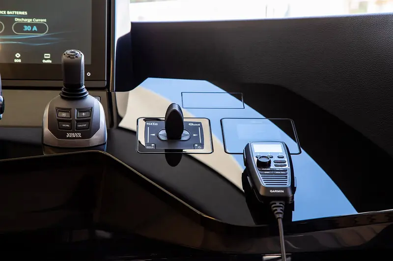 A close-up of a Quick PCST joystick docking control mounted between a Volvo Penta engine interface and a Garmin VHF handset, its hold and power buttons lit