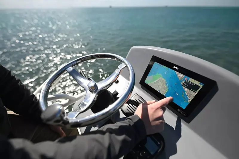 A hand on the wheel and a finger on an Axiom touchscreen chartplotter at the helm, underway.
