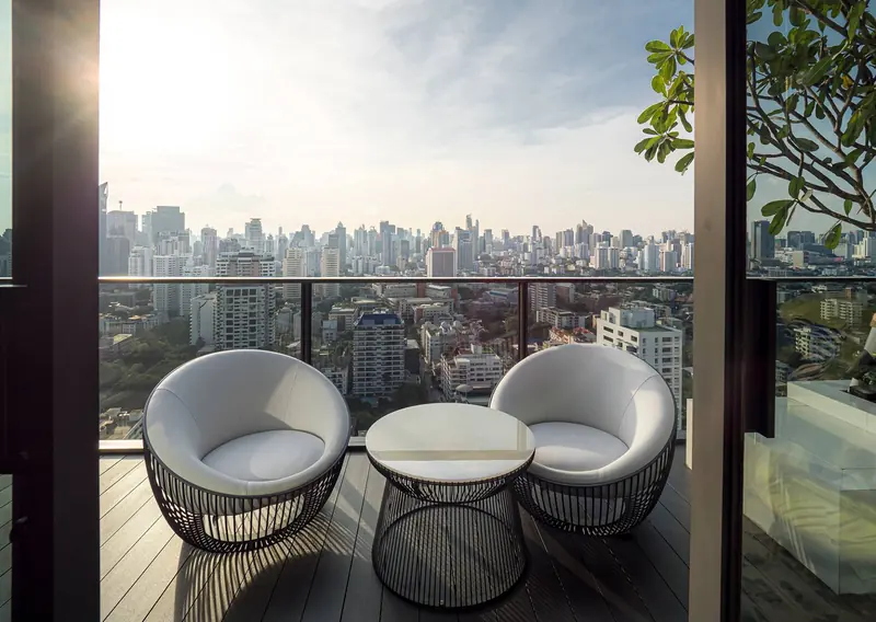 The terrace of the same apartment, with two outdoor tub chairs in a black metal cage frame and a pale stone low table.