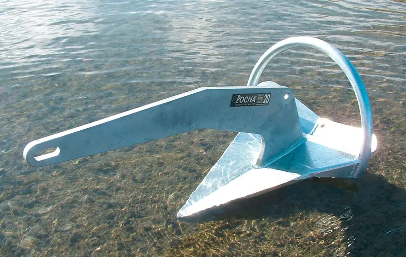A galvanized Rocna 20 sitting in shallow water, tip-weighted fluke down, the shape that self-rights on the seabed