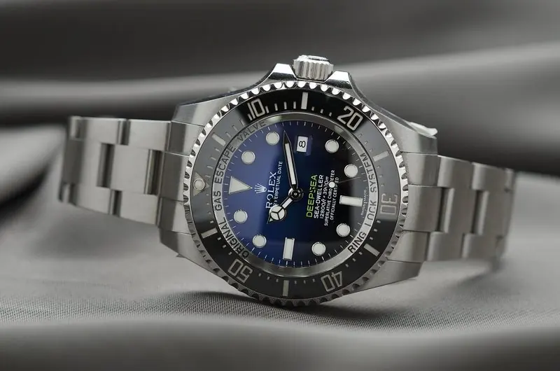 A steel Rolex Deepsea Sea-Dweller rests on grey cloth with its blue dial facing the camera.