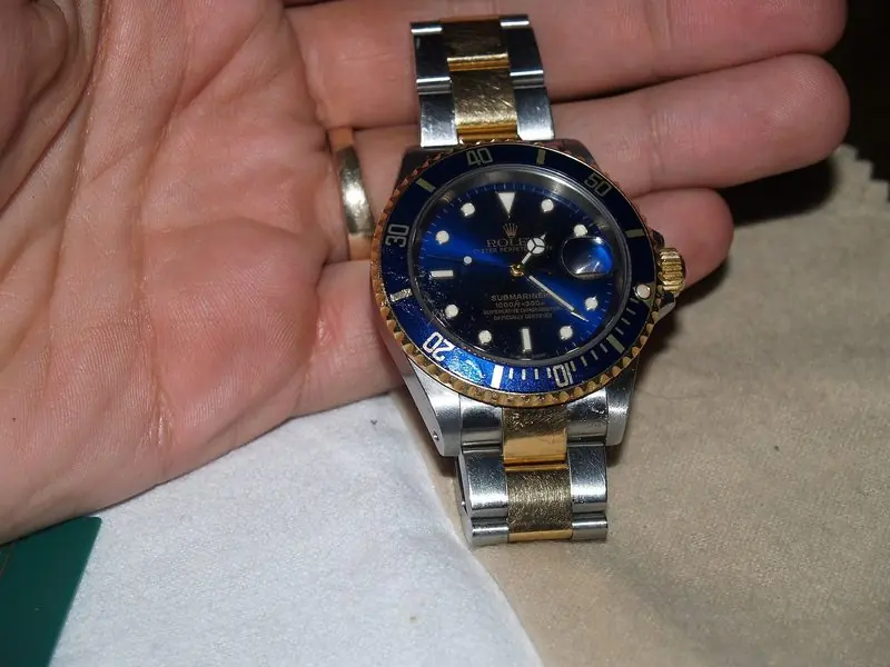 An open hand holds a two tone Rolex Submariner with a blue dial and matching bezel.