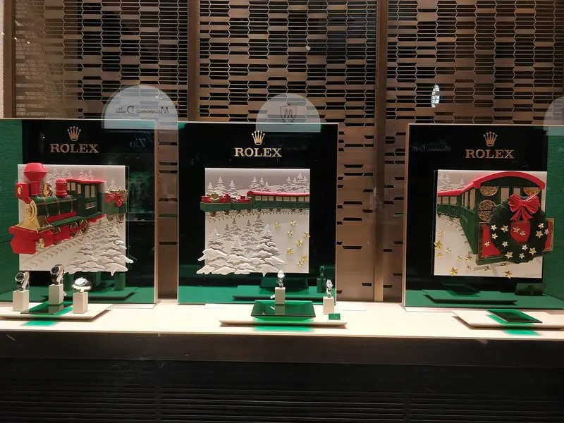 Three window bays carry the Rolex crown above a green Christmas display with watches on small stands.