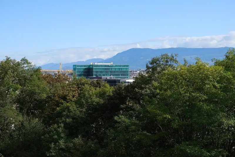 Green glass and stone mark the Rolex headquarters in Geneva, seen across the treetops.