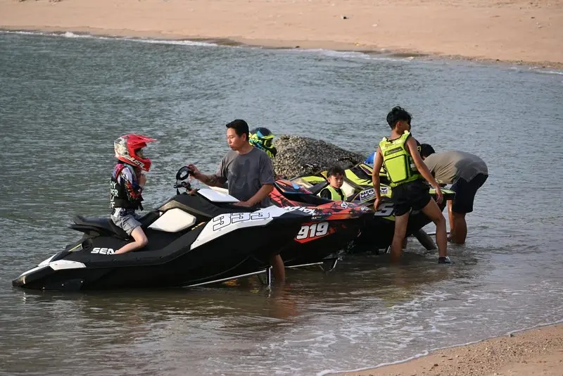 Riders in helmets and buoyancy aids run two Sea-Doo Spark skis down a beach into the shallows.