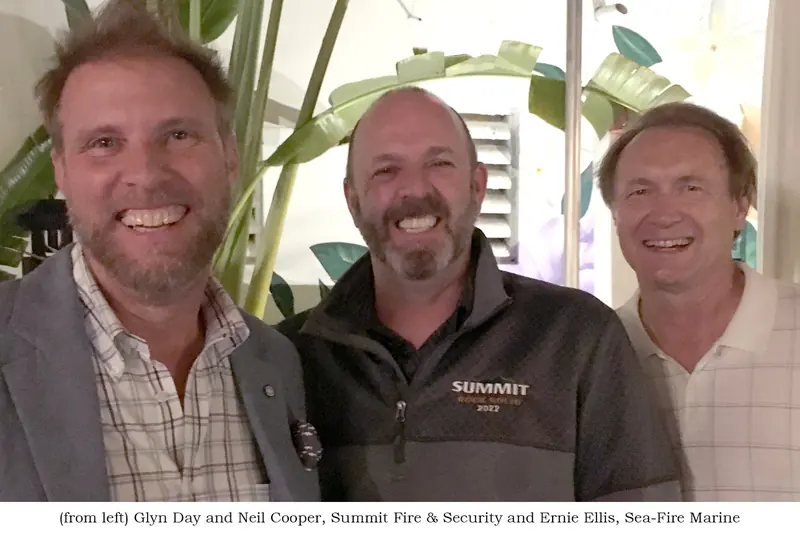 Three men smile for a photo indoors, captioned as Glyn Day and Neil Cooper of Summit Fire and Security with Ernie Ellis, Sea-Fire Marine's president, on the right.