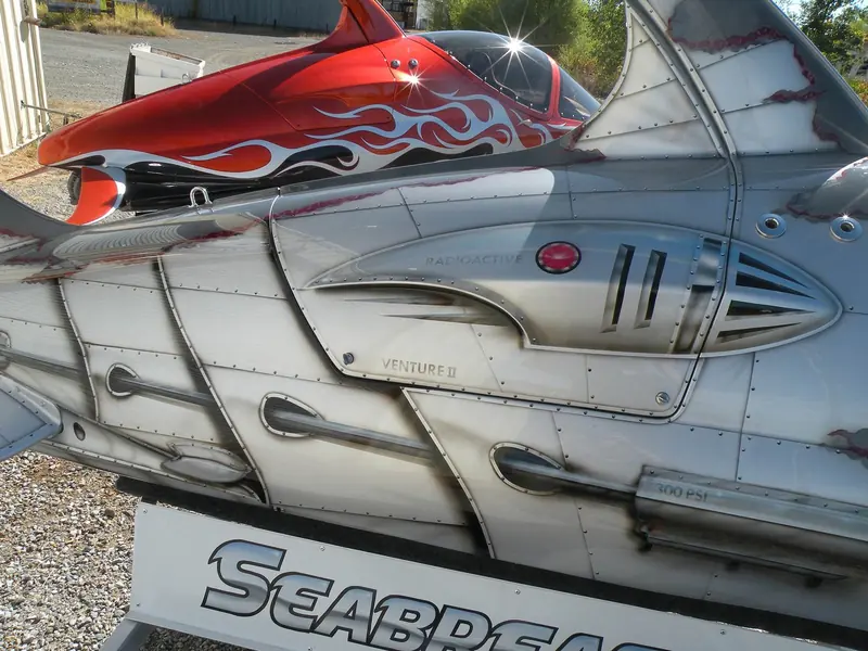 Detail of a flame-liveried Seabreacher's riveted composite hull and canopy, badged Venture II, on its trailer.
