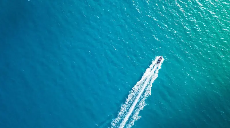 Seen from directly overhead, a single powerboat crosses flat turquoise water and draws a long white wake diagonally across the frame.