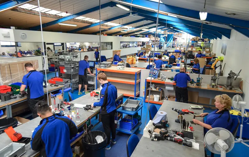 Workers assemble and test safety hardware at benches inside the Cowes factory.
