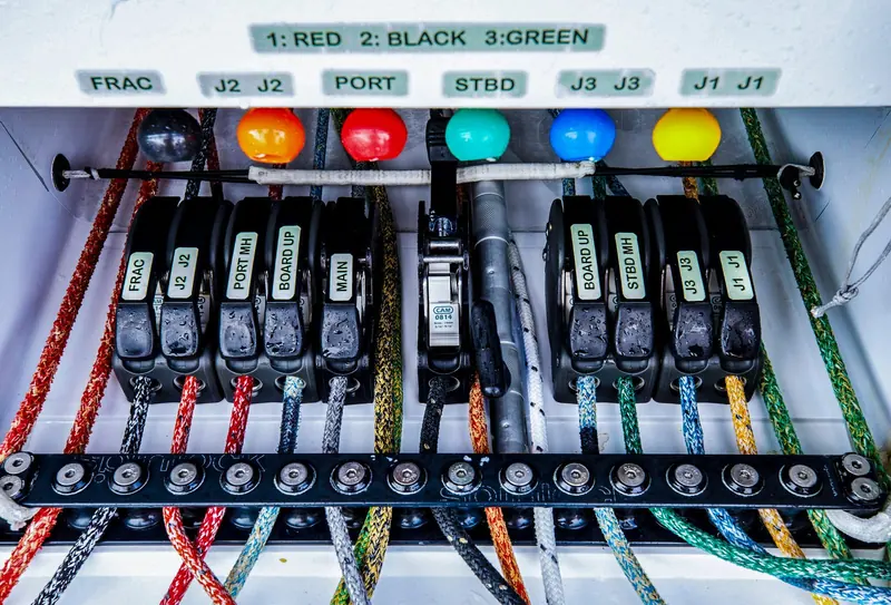 A bank of rope clutches on a rail, each line labelled by function, feeds colour coded sail controls aft to the cockpit.