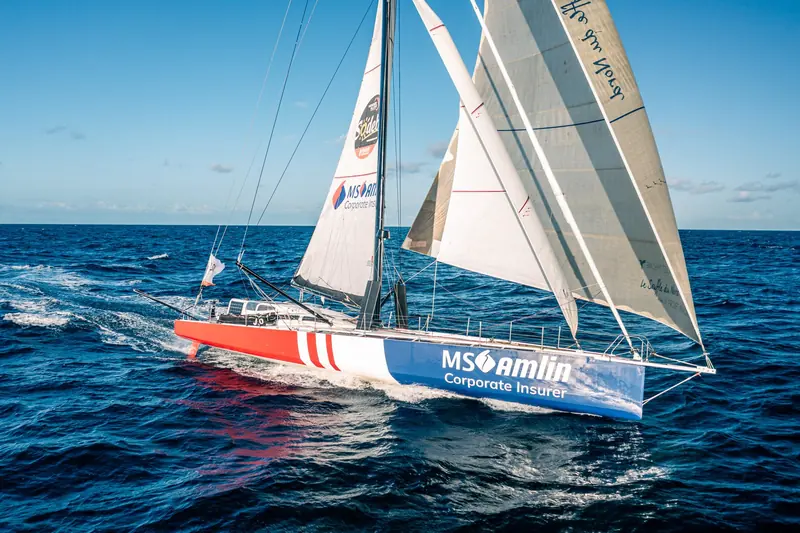 The IMOCA 60 MS Amlin drives to windward under full sail, one of the solo ocean racers whose crews rely on offshore safety gear like this.