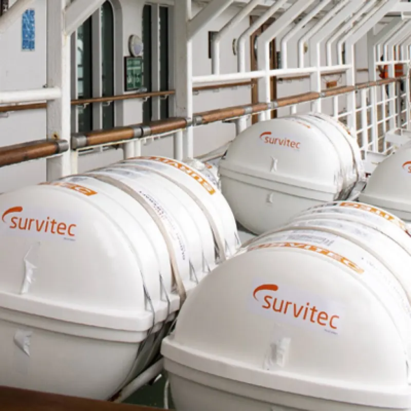Survitec branded liferaft canisters sit in a row on a passenger ship's open deck, each holding an inflatable raft ready for davit launch.