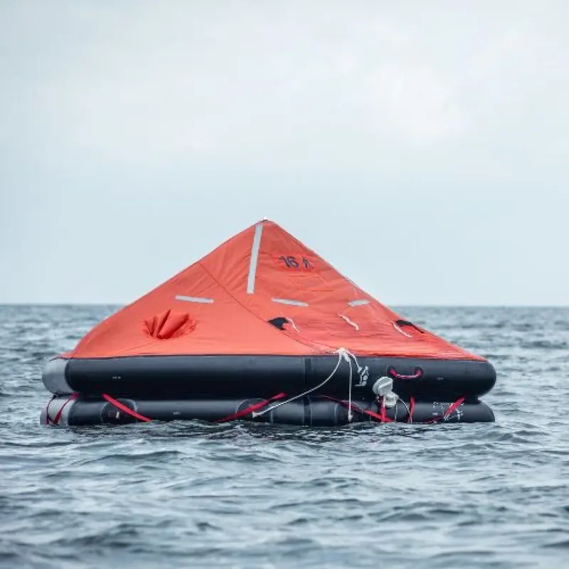 A round throw-over liferaft floats fully inflated on open water, canopy raised and boarding ramp folded against the buoyancy tube.