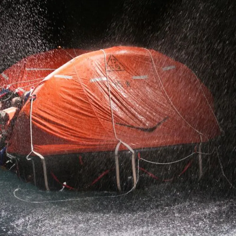 Rain and spray lash a self-righting davit-launch liferaft during a deployment test, the soaked canopy still standing.