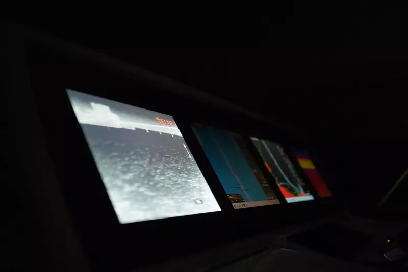 A FLIR thermal camera feed on a multifunction display at the helm at night, showing a dock and open water in white-hot thermal contrast beside chartplotter and sonar screens