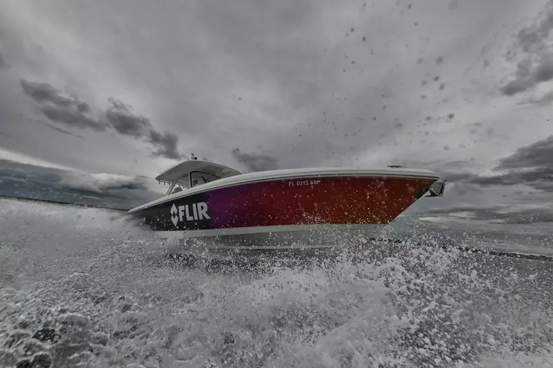 A center console boat painted in FLIR livery runs hard through open water under a stormy sky, spray breaking over the bow