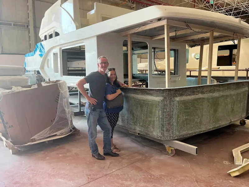 Owners Mark and Fiona stand beside the hull of Awanui NZ, a Nordhavn 51, during construction at the yard before TRAC fin stabilizers were fitted below the waterline.