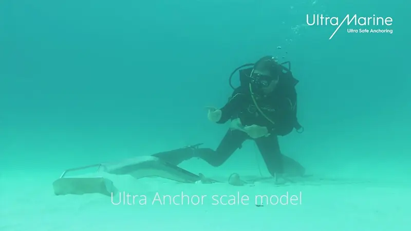 A diver inspects a scale model of the Ultra anchor set on a sandy seabed, demonstrating how the design lands ready to dig in.