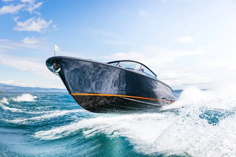 A dark blue Wajer launches off a wave with her bow high and spray flying down both sides.