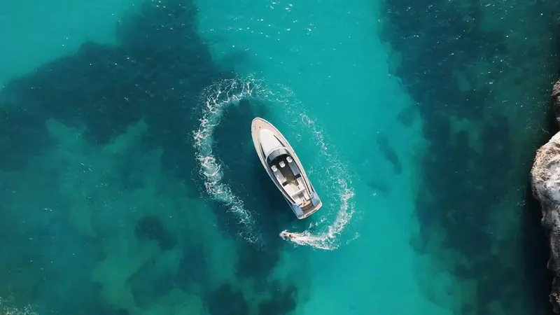 Seen from above, a Wajer carves a tight turn over turquoise shallows and closes the circle of her own wake.