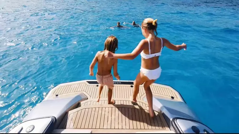 Barefoot on a teak swim platform, a woman and a child look down into clear blue water.