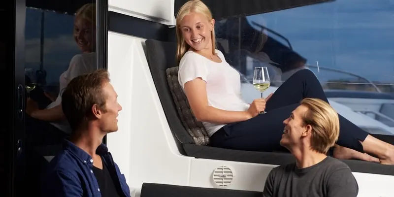 A family relaxes on a flybridge lounge in the evening, warm air moving through a round vent set into the cabin bulkhead below the seat.
