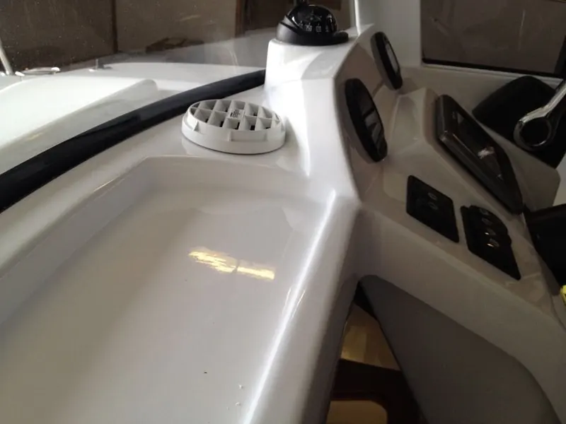 A heater vent sits recessed into a boat's dashboard moulding beside the compass and switch panel.