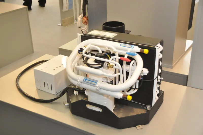 A Webasto BlueCool SC16 self-contained marine air conditioning unit on display, showing the compressor, titanium condenser coil and refrigerant plumbing that would normally be hidden inside a boat's AC compartment