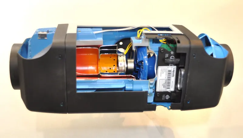 A cutaway Webasto Air Top 3500 forced-air diesel heater, showing the ceramic glow element, combustion chamber and centrifugal blower that draws in cabin air and pushes it out warmed through ducting