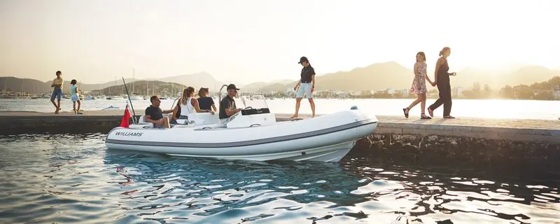 Six guests sit in a Williams tender held against a stone quay as evening light falls over the anchorage.