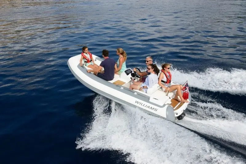 Half a dozen people ride a Williams tender at speed, the hull throwing spray to both sides.