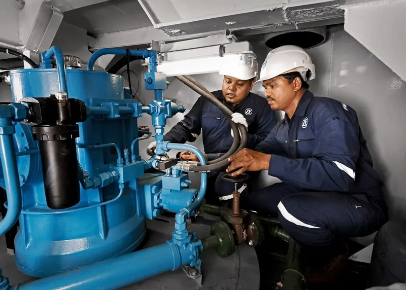 Two ZF-uniformed technicians in hard hats crouch beside a blue-painted hydraulic control unit and valve block in a yacht's engine room, adjusting a manual valve wheel