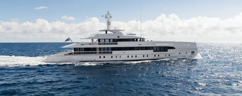 The Heesen hybrid yacht Home under way on a calm sea, her hull name visible amidships and a long wake trailing astern