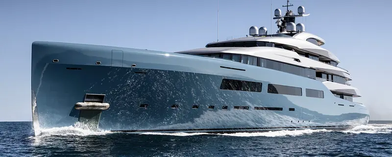 The bow of the yacht Aviva throws spray to both sides as she runs at speed, sunlight catching the wave breaking off her stem