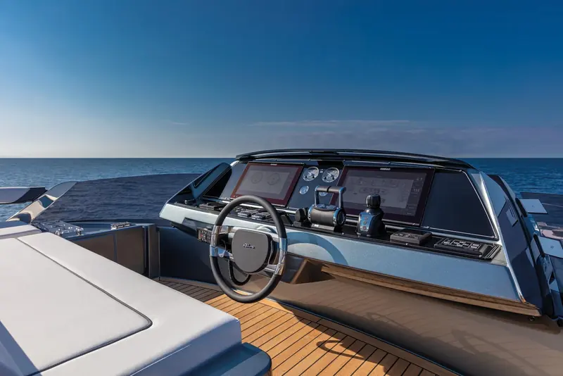 The helm station carries a full-width digital dash ahead of the wheel, with teak decking underfoot.